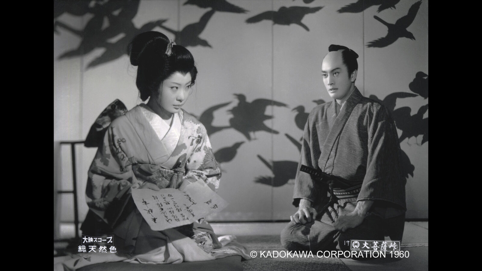 Daibosatsu pass. Svart-hvitt bilde fra japansk film (1960): En kvinne i kimono holder et brev, en mann i tradisjonell drakt sitter ved siden av henne.
