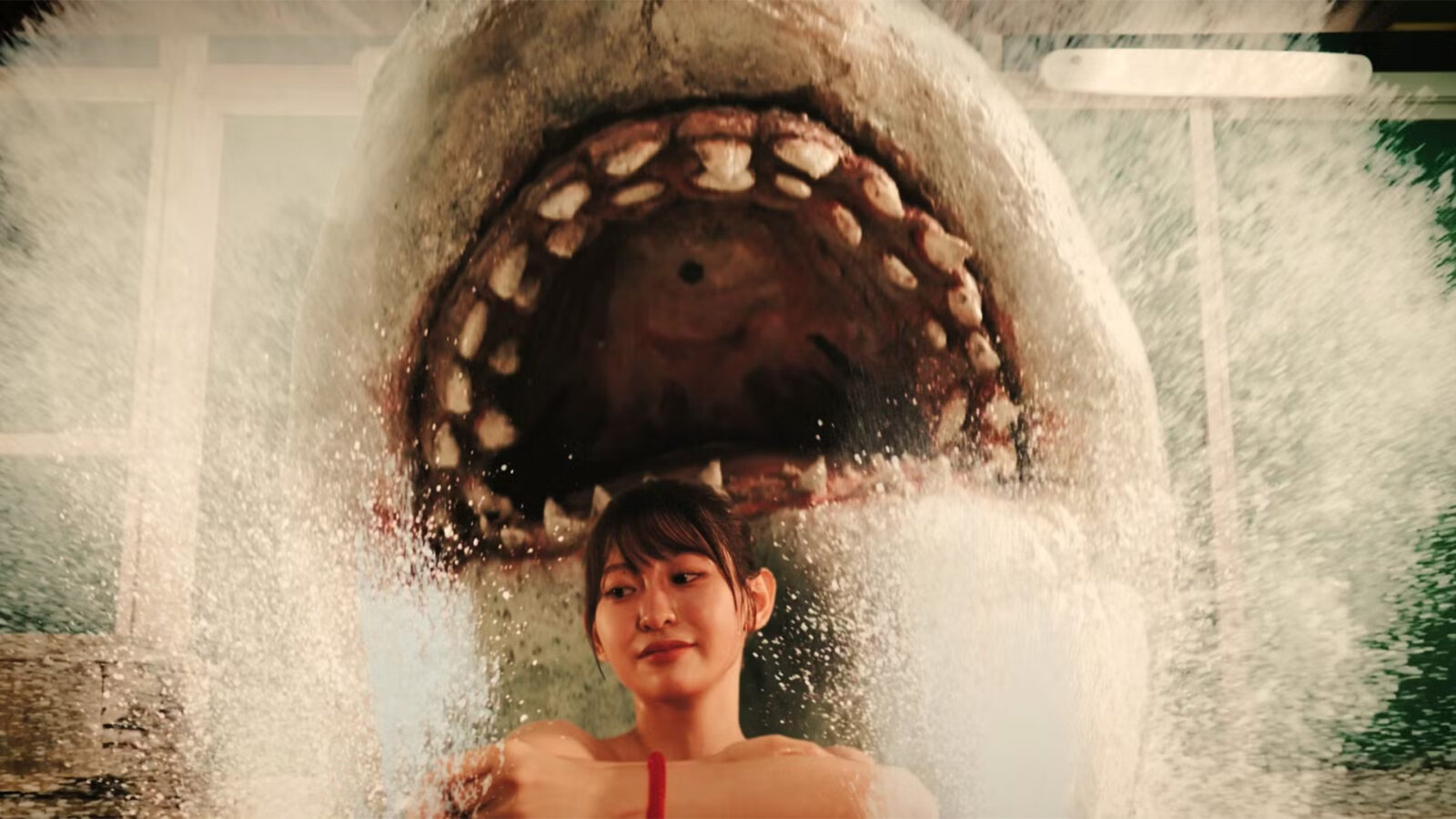 Hot Spring Shark Attack. En kvinne sitter i forgrunnen mens en stor hai hopper opp bak henne med munnen åpen.