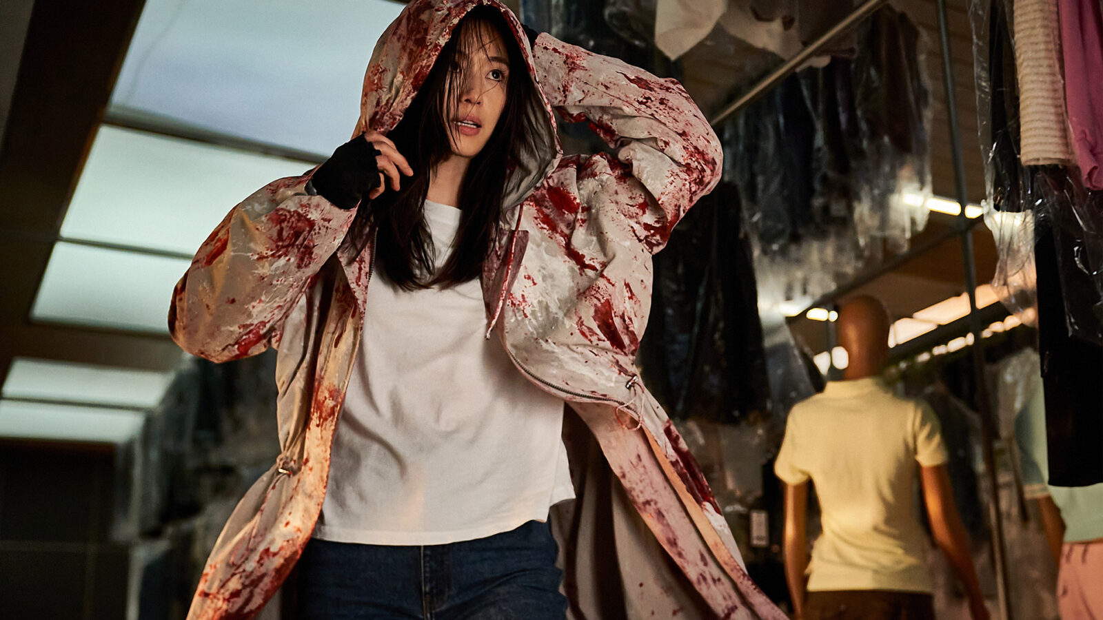 Colony En kvinne i en lys regnfrakk med blodflekker gaar gjennom en klesbutikk mens hun holder i hetten