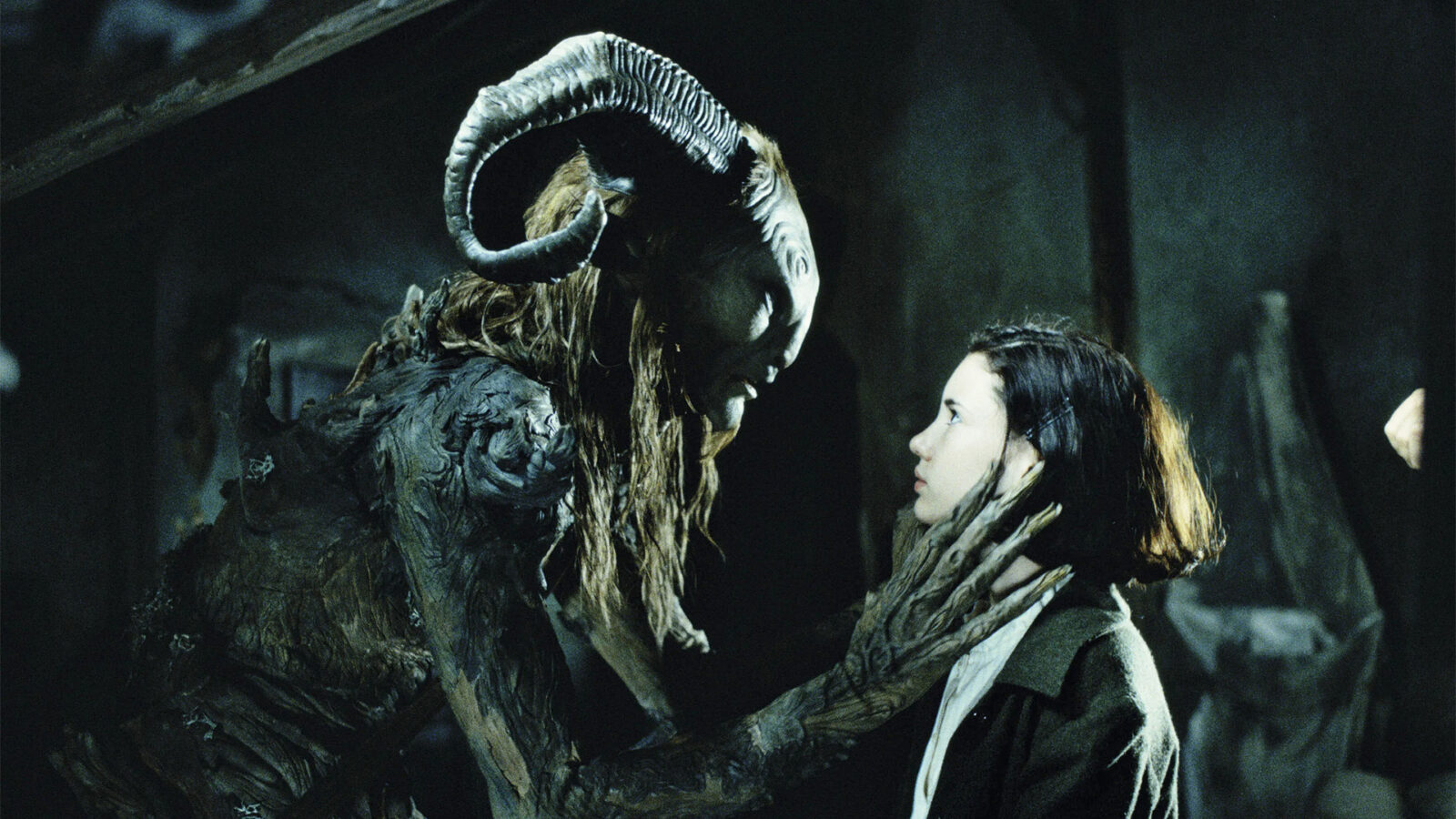 Pans Labyrinth En stor menneskelignende skapning med store buede horn holder en jente forsiktig rundt ansiktet med begge hendene De staar tett overfor hverandre og ser hverandre inn i oeynene i moerke omgivelser
