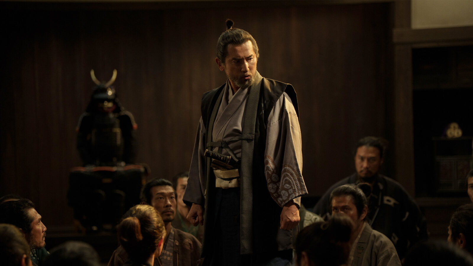 The Samurai and the Prisoner En mann i tradisjonell japansk drakt staar i et rom med flere personer Bak ham er en samurairustning utstilt