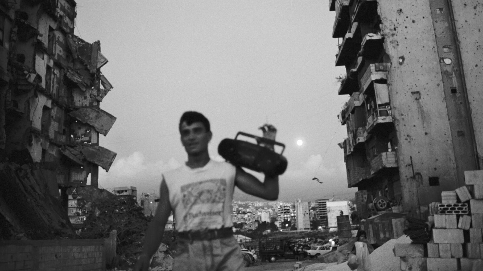 Do You Love Me Mann bærer en boomboks mellom to ødelagte boligblokker Ruiner og bygninger i bakgrunnen