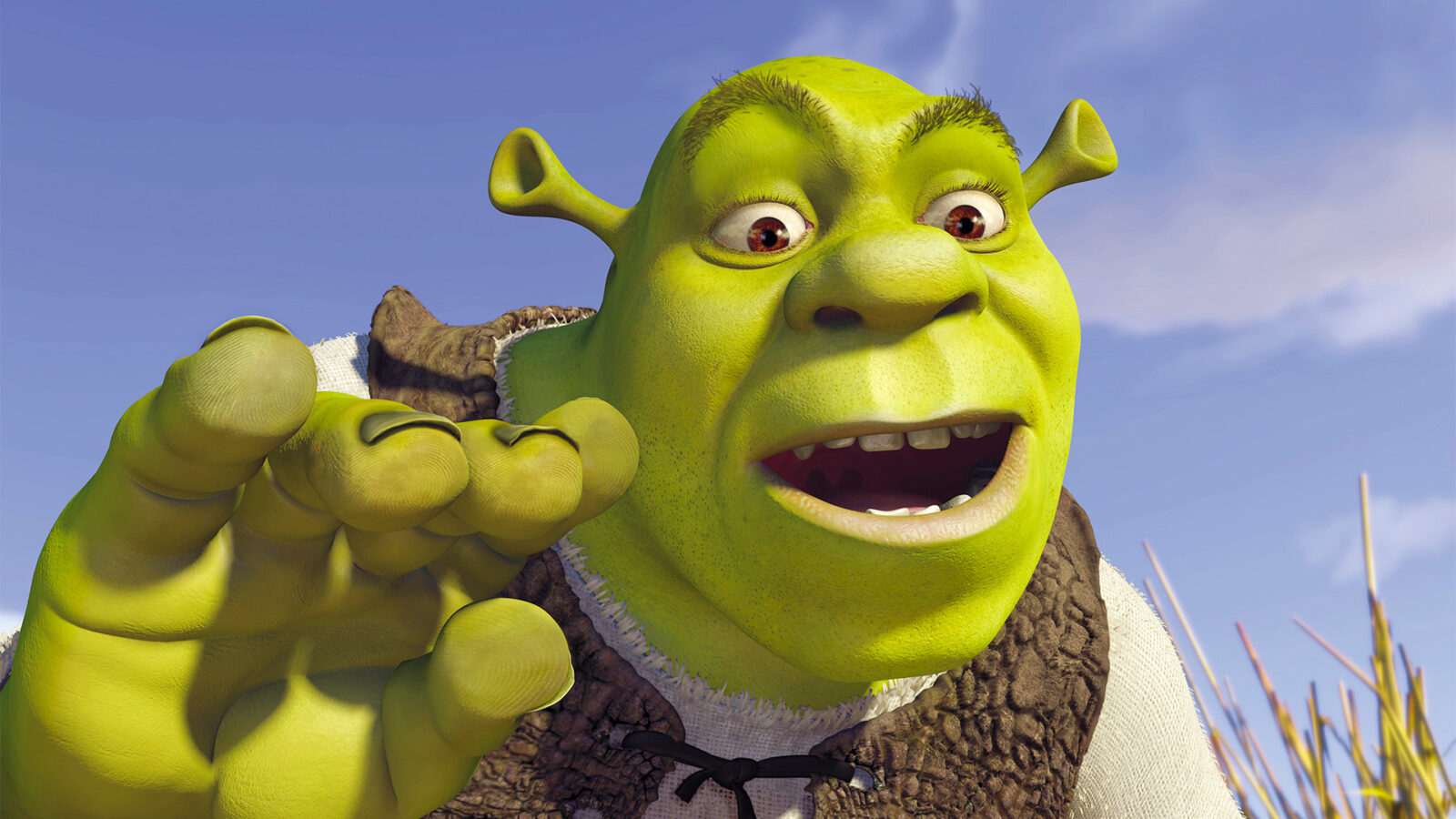 Shrek En grønn animert figur med store ører og brun vest vises nærbilde mot blå himmel Figuren har åpen munn og holder en hånd opp foran seg