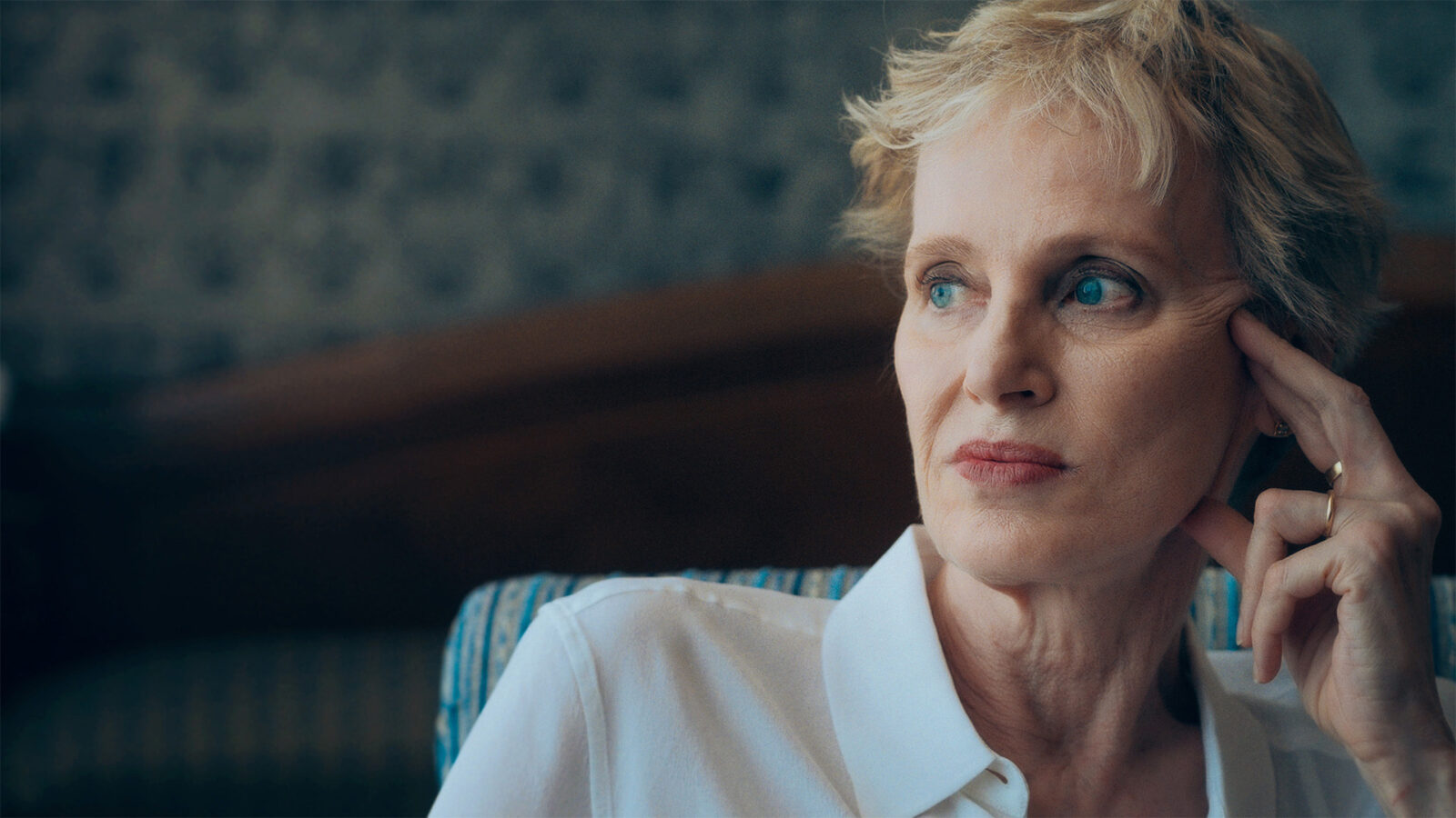 Siri Hustvedt Dansen rundt selvet En kvinne med kort lyst hår og hvit skjorte sitter i en stol Hun ser til siden og har hånden mot tinningen