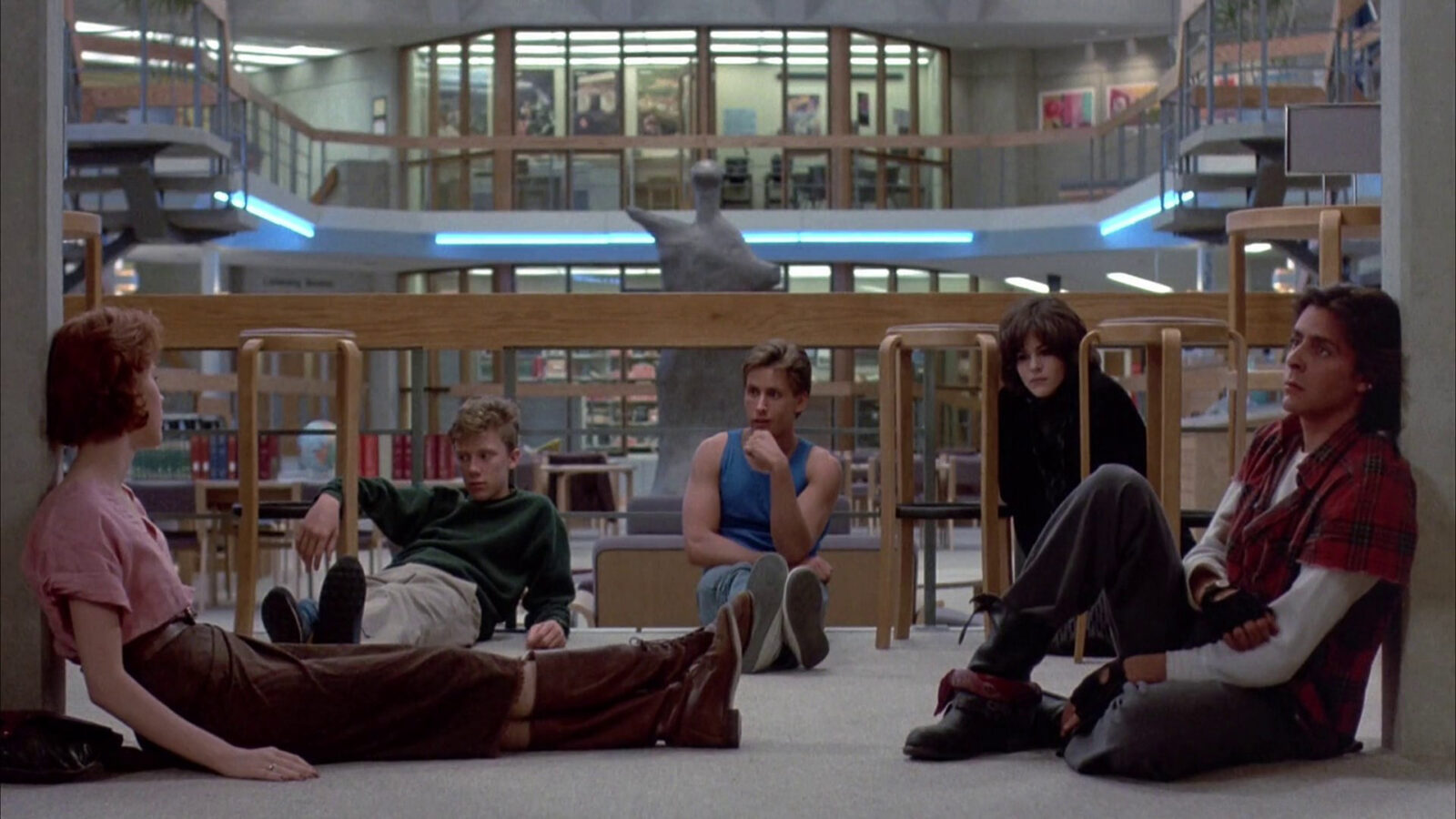 The Breakfast Club fem unge personer sitter på gulvet i et bibliotek Det er stoler rundt dem og en stor statue i bakgrunnen