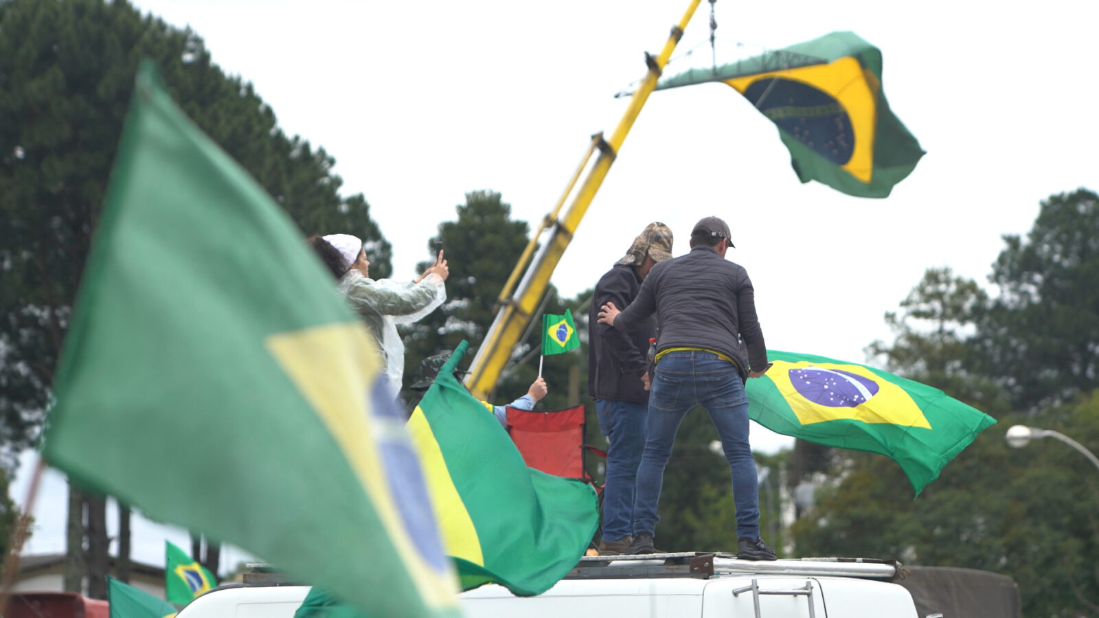 DKR At This Moment. Bildet viser en gruppe mennesker som vifter med brasilianske flagg, trolig under en demonstrasjon eller feiring i Brasil.