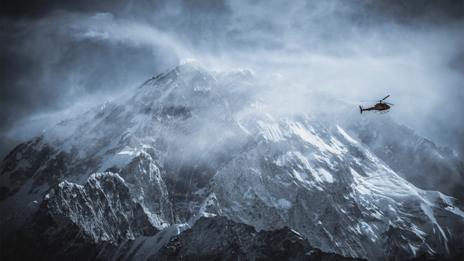 DKR Everest Dark. Bildet viser et snødekt fjell, trolig Mount Everest, med et helikopter som flyr nær toppen.