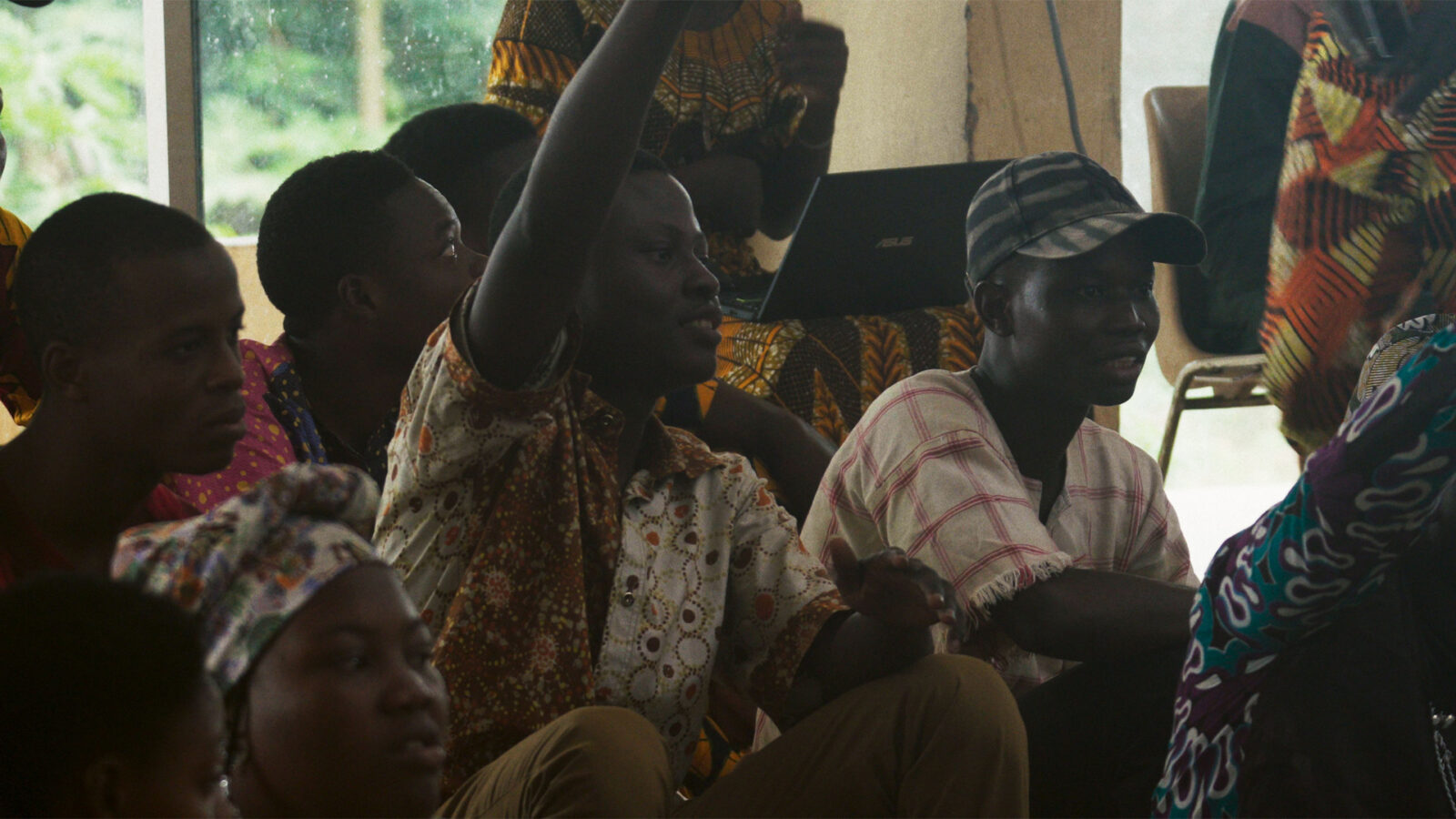 Dahomey Nasjonalmuseet. Bildet viser en gruppe unge mennesker i diskusjon eller undervisning, hvor én person rekker opp hånden for å delta aktivt.
