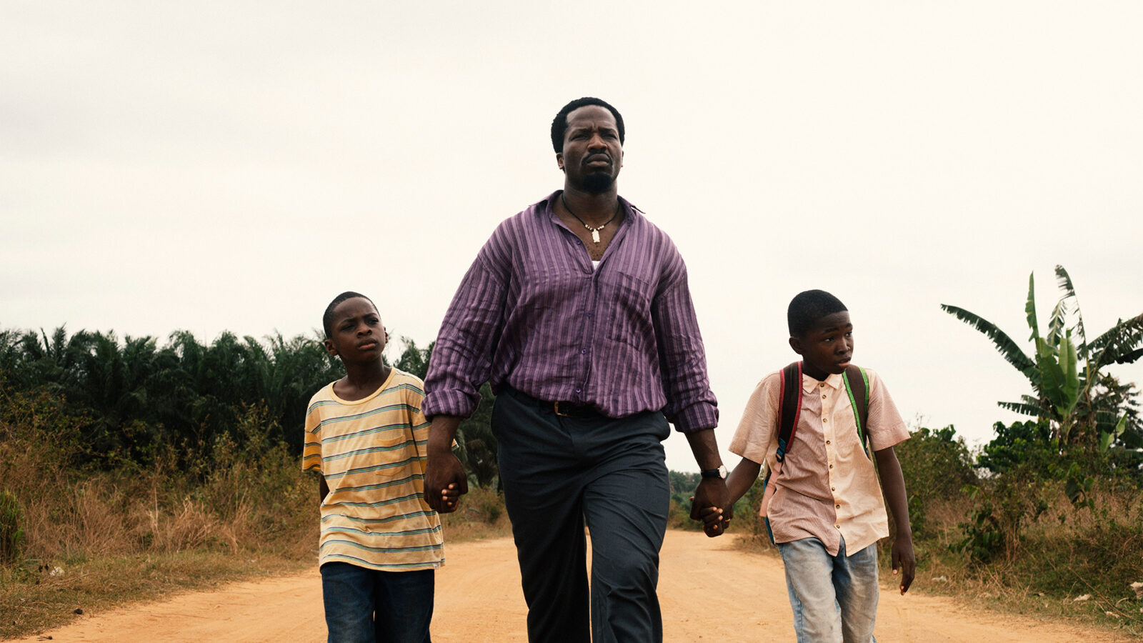 Nollywood kveld. Bildet viser en voksen mann og to gutter som går sammen på en landevei i et landlig område, trolig på vei et sted.