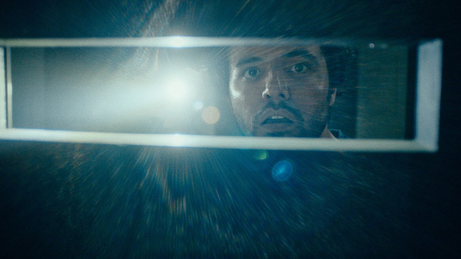 Kortfilmsalong Ingensteds En mann ser gjennom en smal åpning med en lommelykt